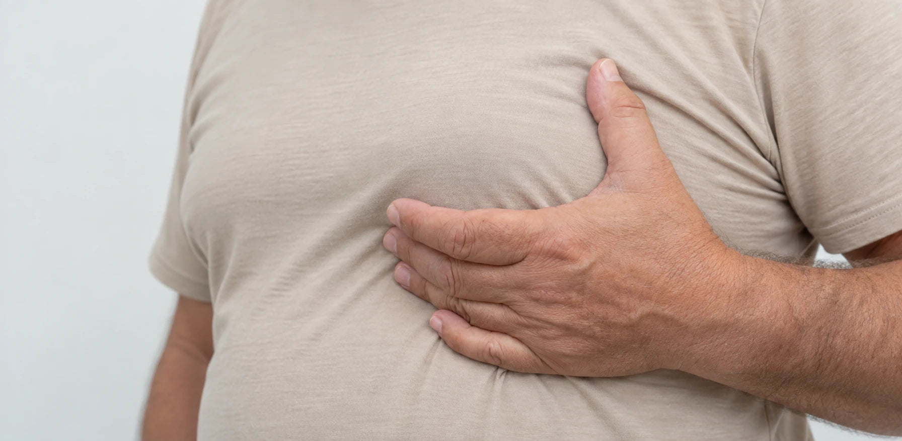 Closeup of a man checking how a regular sand colored shirt sits across his chest.